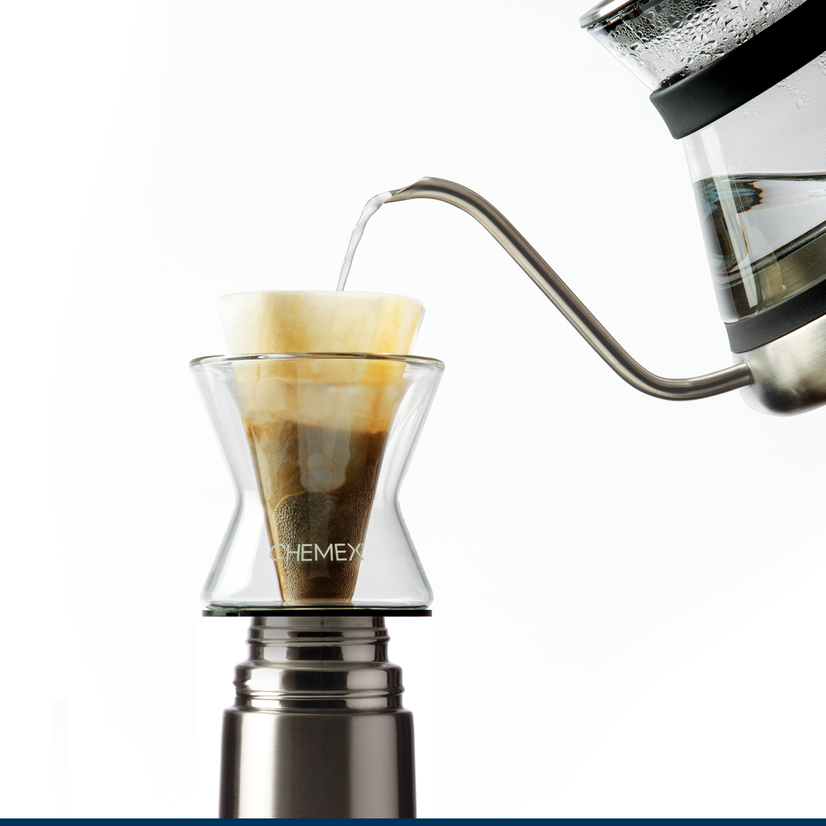 En Chemex Tragt Filter-Drip 1-kop, elegant suppleret med en hældekedel, forfiner kaffebrygning. Denne opsætning med et papirfilter og kaffegrums sidder på en metallisk base mod en hvid baggrund.