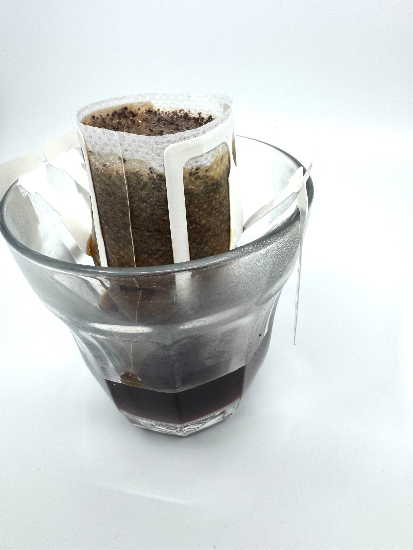 En enkelt servering (w) pour-over-opsætning fra EverBean er placeret på et klart glas med et papirfilter af specialkaffe-grums klippet til dets kanter. Brygget kaffe drypper nedenunder mod en almindelig hvid baggrund, hvilket viser bryggemetodens enkelhed og elegance.