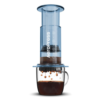 En Clear Limited AeroPress kaffebrygger fra Aeropress, lavet af slidstærkt Tritan™ med en subtil blå nuance, sætter sig elegant over et glaskrus for at fremvise den rige mørke kaffeoplevelse, som den drypper nedenunder.