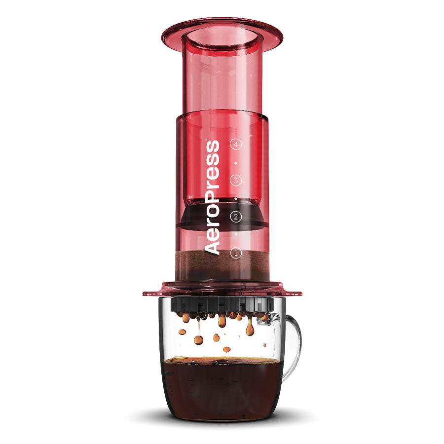 AeroPress, Clear Kaffebrygger, Rød-limited kaffemaskinen fra Aeropress er sat over et klart glaskrus. Dens 3-i-1 bryggeteknologi er lavet med holdbart Tritan™ og drypper kaffen yndefuldt ned i kruset, mens det ikoniske AeroPress-logo pryder dets elegante design.