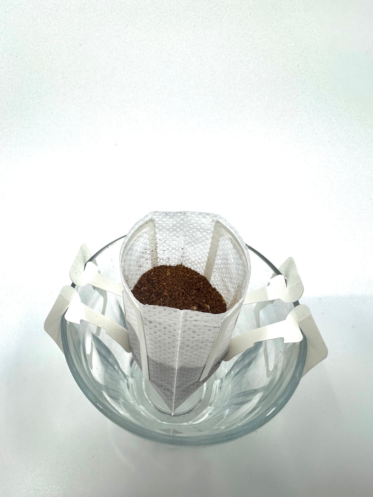 Et glaskrus rummer et Single Serve (w) papirdryp kaffefilter med EverBean's Specialkaffe, klar til brygning. Filteret er perfekt suspenderet over kruset, klar til at byde varmt vand velkommen og levere en rig kaffeoplevelse.