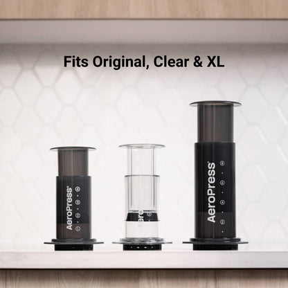 Tre AeroPress-kaffemaskiner – Original, Clear og XL – er pænt arrangeret på en hvid bordplade mod en sekskantet fliseplade. AeroPress Organizer fra Aeropress tilbyder en ideel køkkenbordløsning til kaffepresseopbevaring, der sikrer, at alt passer problemfrit.