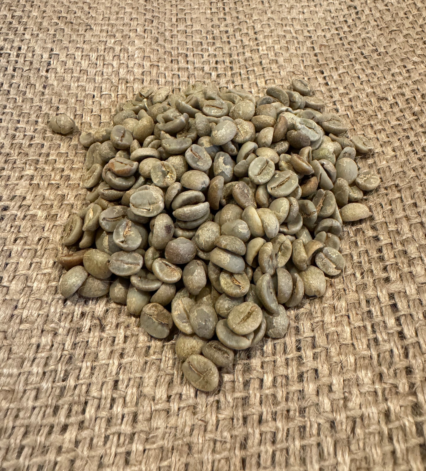 En bunke EverBeans 401 · Colombia, Grønne Bønner, Koffeinfri hviler på vævet jute. De små, ovale bønner viser en let grøn nuance mod det strukturerede brune stof.