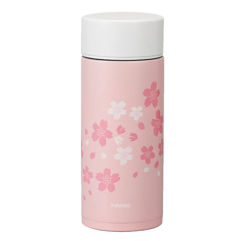 Hario Stick Bottle 350mL Sakura kan prale af kirsebærblomster i hvid og mørk pink på en elegant pink krop med hvidt låg, perfekt til drikke på farten. Mærket "Hario" er elegant printet i bunden.