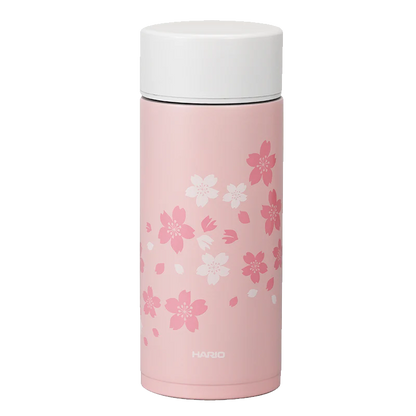 Hario Stick Bottle 350mL Sakura kan prale af kirsebærblomster i hvid og mørk pink på en elegant pink krop med hvidt låg, perfekt til drikke på farten. Mærket "Hario" er elegant printet i bunden.