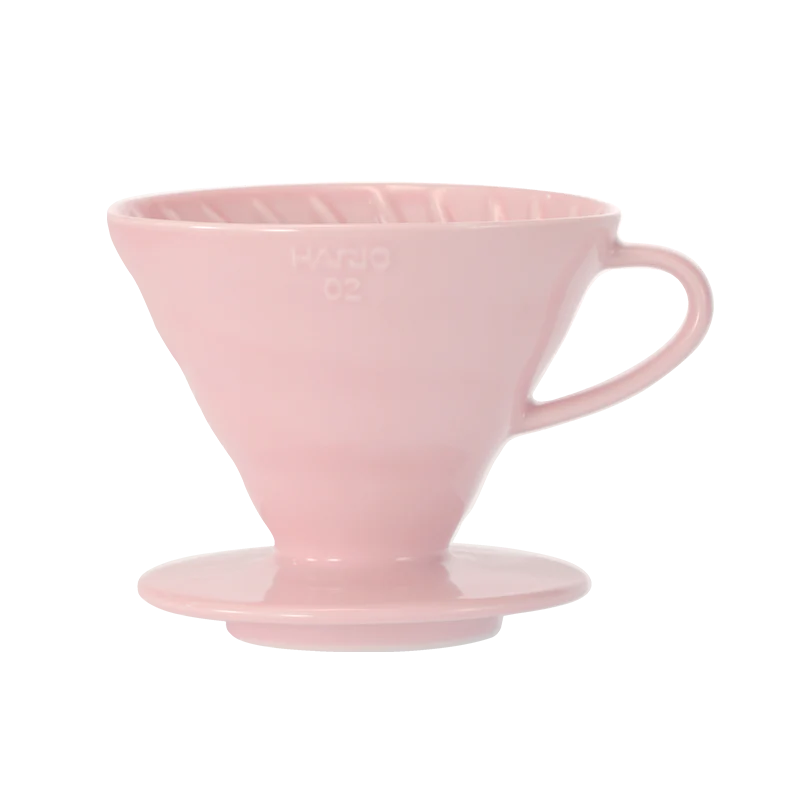 Hario Keramisk Drip Tragt i pink, der ligner en V60, inkluderer ribbede indvendige vægge for optimal kaffeekstraktion og en udspændt bund. Dens håndtag sikrer nem brug under manuelle brygningssessioner.