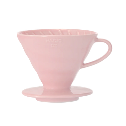 Hario Keramisk Drip Tragt i pink, der ligner en V60, inkluderer ribbede indvendige vægge for optimal kaffeekstraktion og en udspændt bund. Dens håndtag sikrer nem brug under manuelle brygningssessioner.