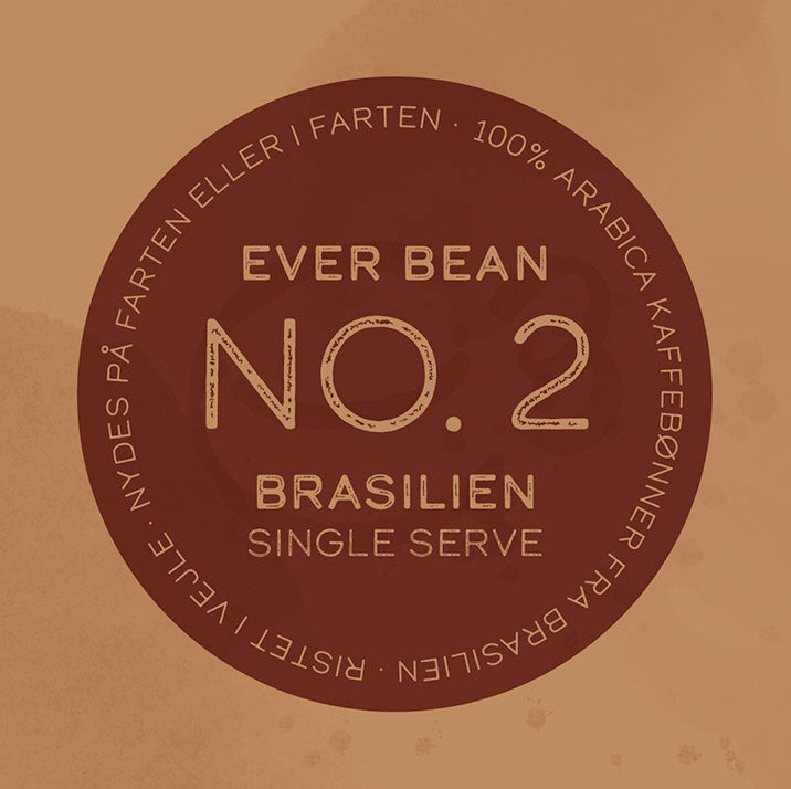 En cirkulær etiket på Single Serve (w)-produktet fra EverBean viser "No. 2, Brasilien, Single Origin kaffe." Dansk tekst lyder: "100% Arabica kaffebønner fra Brasilien, Ristet i Norge. Nydes som Specialkaffe på farten eller i farten," sat mod en rig brun baggrund.