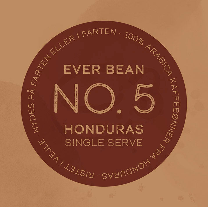 En cirkulær kaffeetiket på en brun baggrund lyder "EverBean No. 5, Honduras, Single Serve (w)." Langs kanten står der "100% Arabica kaffebønner fra Honduras" og "Ristet i Vejle - Nydes på farten eller i farten," der fejrer denne Single Origin kaffe som udsøgt Specialkaffe.